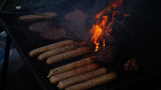 A barbecue grill with several sausages and burger patties cooking over open flames and darkened areas of smoke.