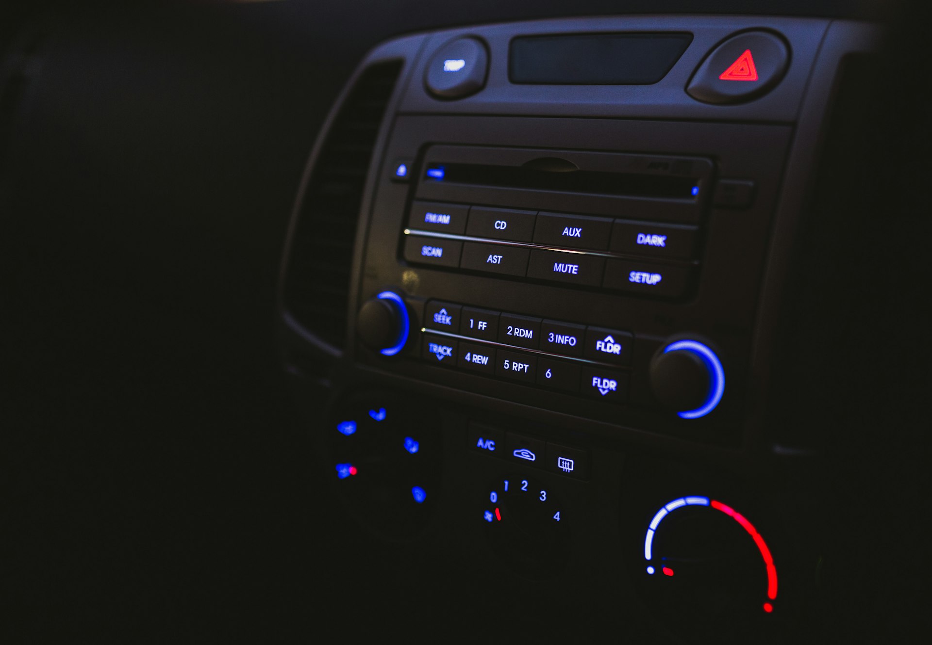 Nahaufnahme eines eingeschalteten Car-HiFi-Radios mit blauen LED-Tasten und Klimaanlagenreglern im Dunkeln