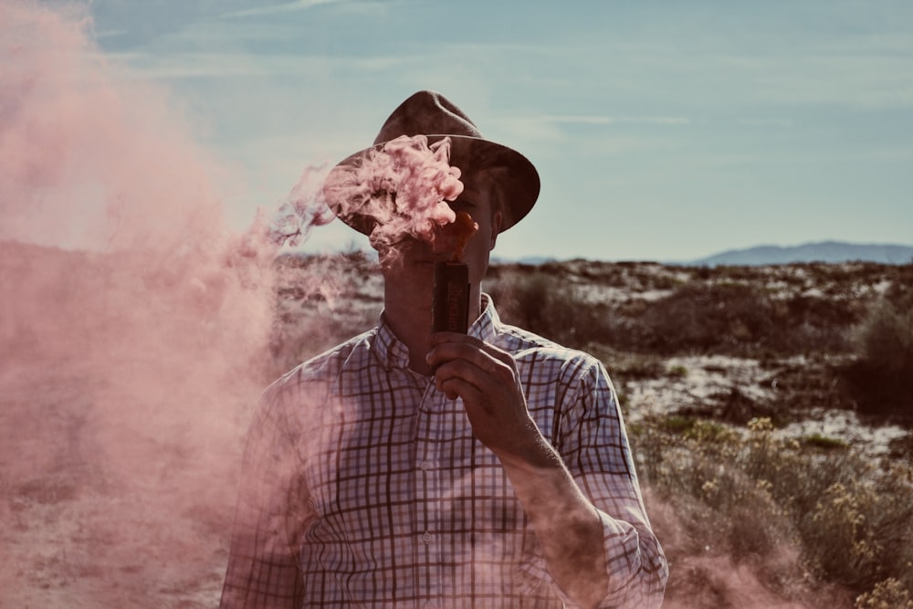 man standing on open field holding device with smoke during daytime