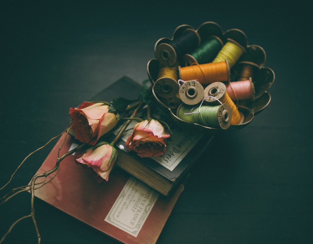 assorted-color thread in bowl beside three roses on two hardbound books