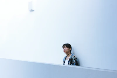 Model wearing an ultra-minimalist jacket standing against a stark white wall with soft shadows.