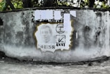 A weathered concrete wall displays a stencil portrait, surrounded by election-themed graphics. Above the portrait, several papers are attached to the wall, likely serving as notices or posters.