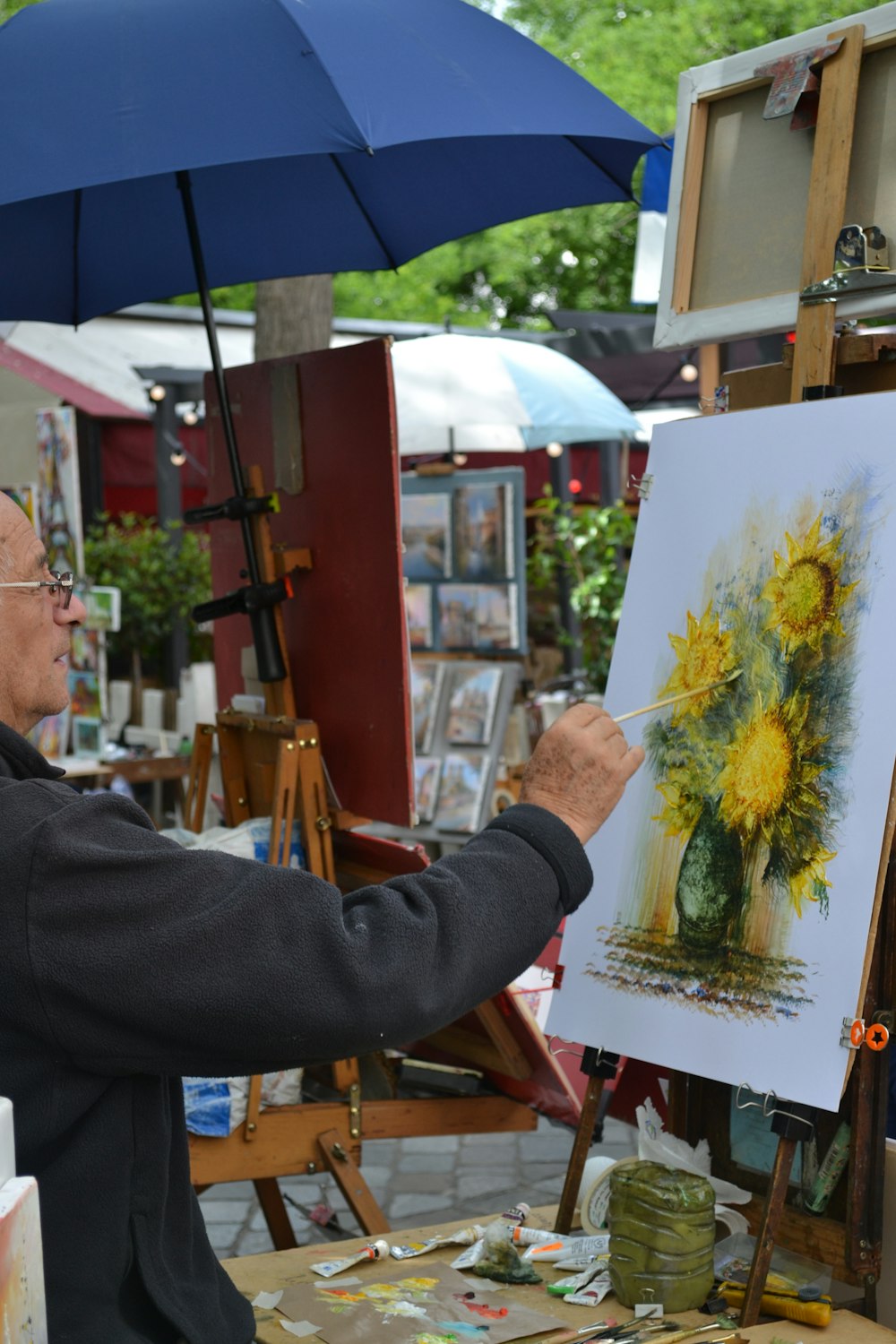 a man painting a picture with a blue umbrella