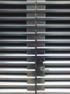 A metallic or aluminum louvered door with horizontal slats and a silver handle on one side. The door is symmetrical and provides a sleek, industrial aesthetic.