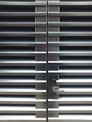 A metallic or aluminum louvered door with horizontal slats and a silver handle on one side. The door is symmetrical and provides a sleek, industrial aesthetic.