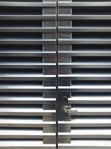 A metallic or aluminum louvered door with horizontal slats and a silver handle on one side. The door is symmetrical and provides a sleek, industrial aesthetic.