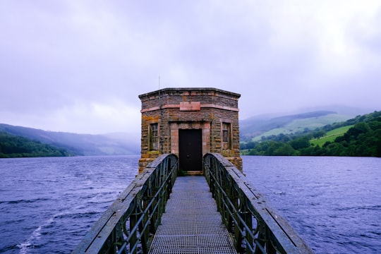 black metal bridge leading to building surrounded by water in Talybont Reservoir United Kingdom