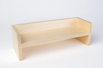 A minimalist, light-colored wooden bench with simple, modern lines. The bench is constructed from layered plywood, showcasing its layered edges. It has a rectangular seating surface with raised back and side panels, and an open space underneath.
