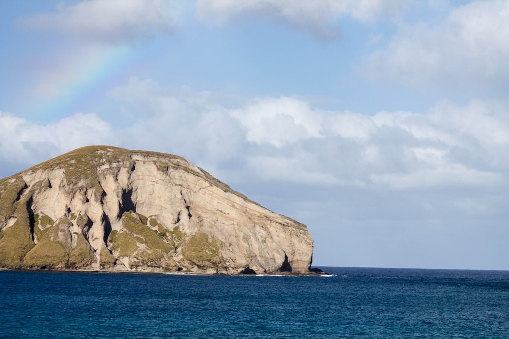 A large rock hill surrounded by a cloudy sky over top of the ocean.