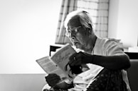 An elderly person happily reading a book in a sunlit room.