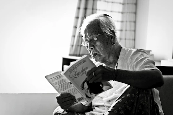 A friendly caregiver reading a book to an elderly client in a sunlit room.