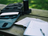 An open notebook and pen on a wooden table outdoors.