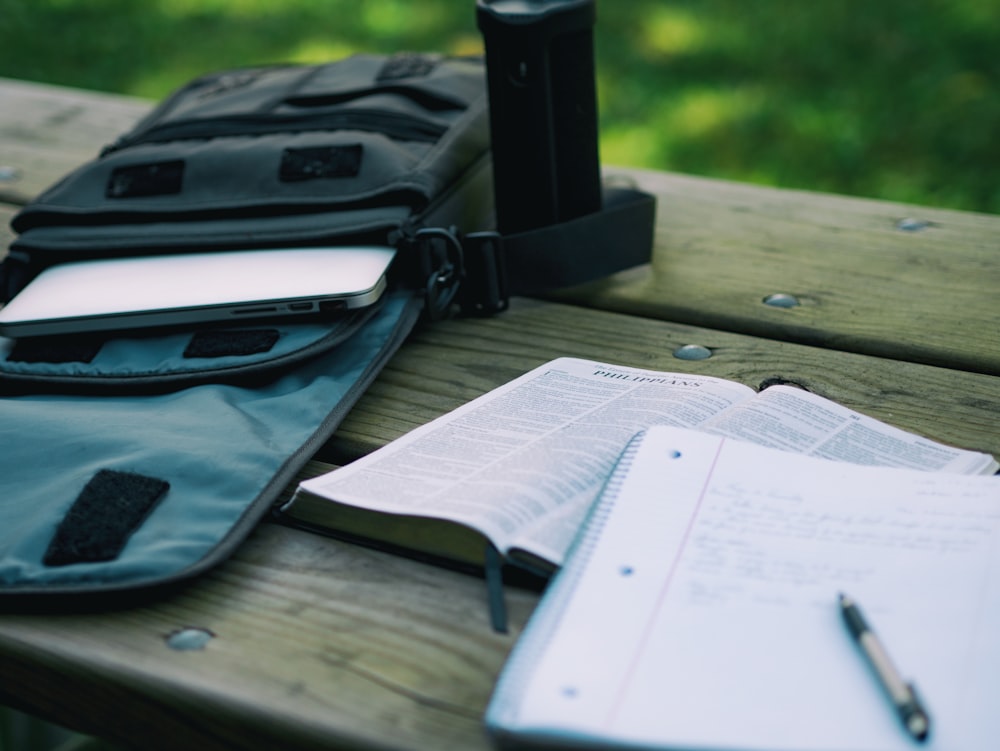 A notebook and a Bible on a bench next to a bag with a laptop