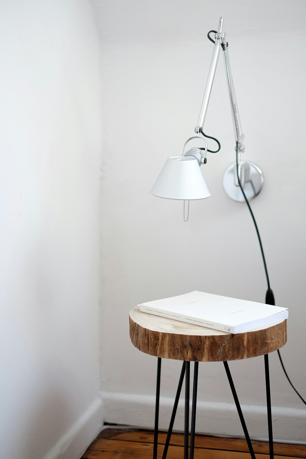 Support de lampe de bureau gris sur le mur blanc sous le tabouret marron avec un livre blanc sur le dessus près du coin du mur