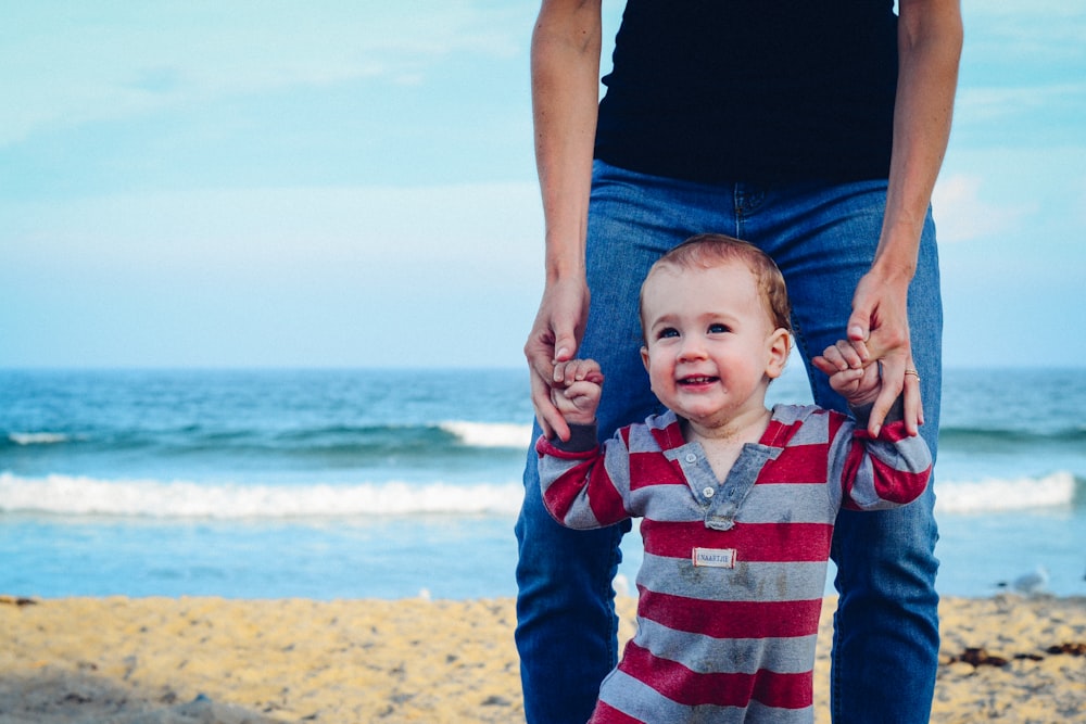 man assisting baby to walk on beach