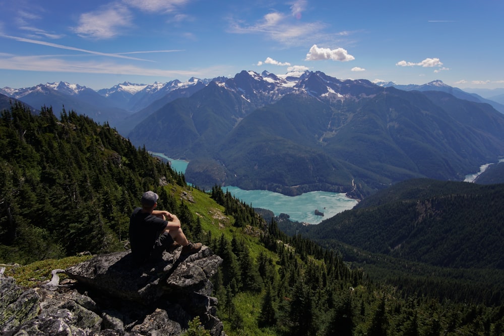 person sitting on rock formation facing landscape