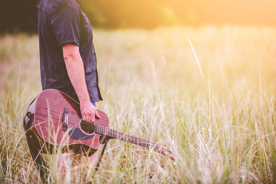 man carrying brown cutaway acoustic guitar standing on green grass field