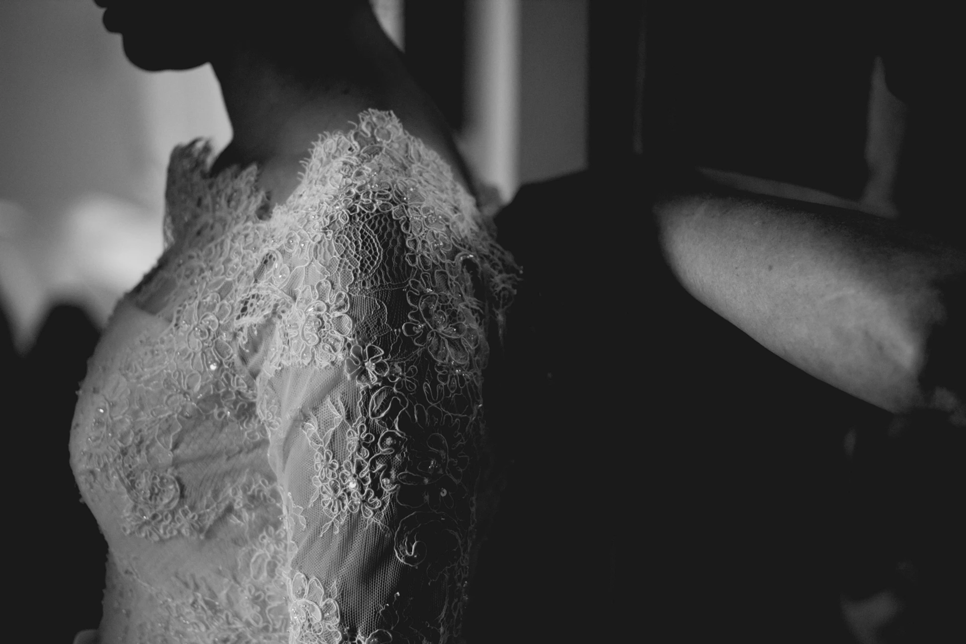 A dramatic black and white photo capturing the delicate details of a bride's lace dress and hands.