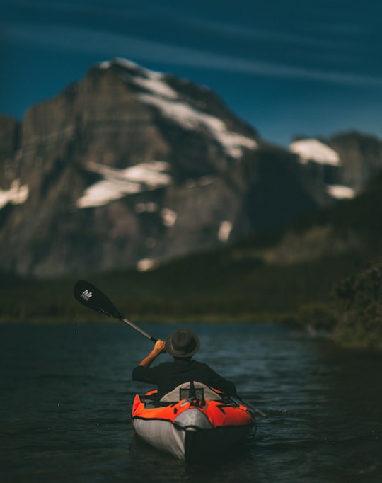 man riding on inflatable kayak beside mountain in Swiftcurrent Lake United States
