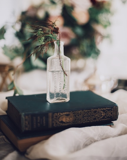 Close-up of a delicate glass bottle filled with a golden botanical elixir, surrounded by fresh herbs and flowers.