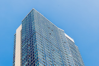 A modern high-rise building with glass windows reflecting the sky.