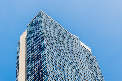 A modern high-rise building with glass windows reflecting the sky.