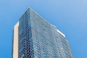 A modern high-rise building reflecting sunlight against a clear blue sky.