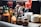 A collection of various sauces, spices, and condiments arranged on a table. There are multiple bottles of hot sauce, including brands like Tabasco and Sriracha, alongside jars of crushed red pepper and utensils. Stacks of small white plates are also visible, adding to the organized appearance of the dining setup.