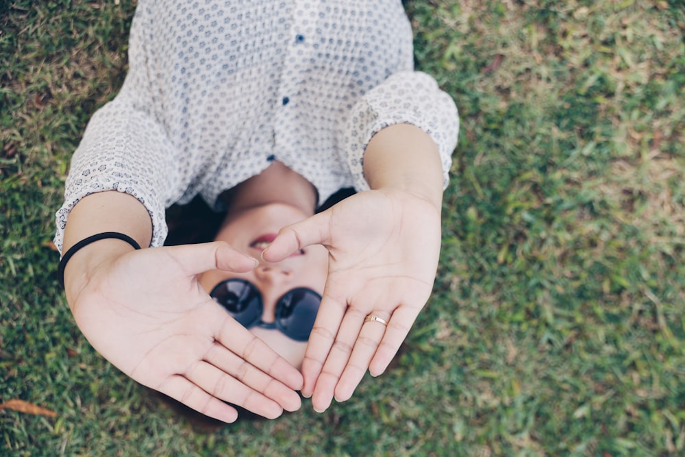امرأة مستلقية على العشب تشكل يديها على شكل مثلث أثناء النهار