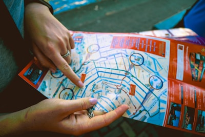 Two hands are holding and pointing at a colorful city map. The map contains various streets, landmarks, and highlighted routes. Important points are circled in blue, with sections of the map bordered in red.