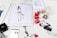 A workspace is filled with feminine fashion illustrations and cosmetic items. Digital drawings are displayed on tablets alongside traditional sketches. Nail polish bottles in various vibrant colors and a Dior makeup box are arranged neatly. The scene blends technology and art in a stylish manner.