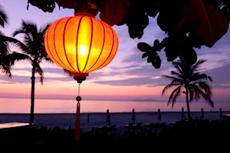 A cozy night beach scene with tiki torches glowing softly under colorful Japanese lanterns and a subtle rainbow glow reflecting the LGBTQIA theme.