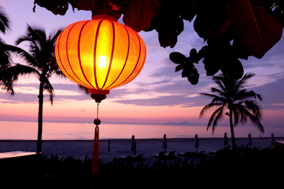 A cozy night beach scene with tiki torches glowing softly under colorful Japanese lanterns and a subtle rainbow glow reflecting the LGBTQIA theme.