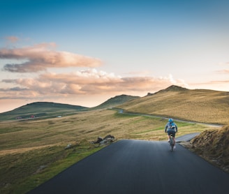 person cycling on road distance with mountain during daytime