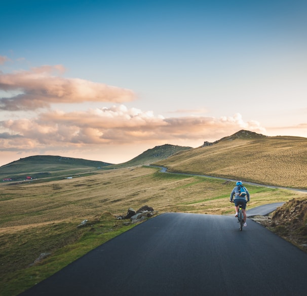 person cycling on road distance with mountain during daytime