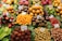 A vibrant display of various fruits and colorful produce, neatly arranged with labels indicating their names and origins. The assortment includes starfruits, naranjillas, rambutans, passion fruits, and more, accompanied by a bottle of juice or syrup. The fruits are placed on green leafy backdrops, enhancing their freshness and appeal.