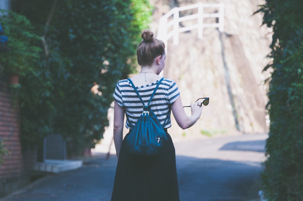 woman in striped shirt with backpack holding sunglasses while walking on street