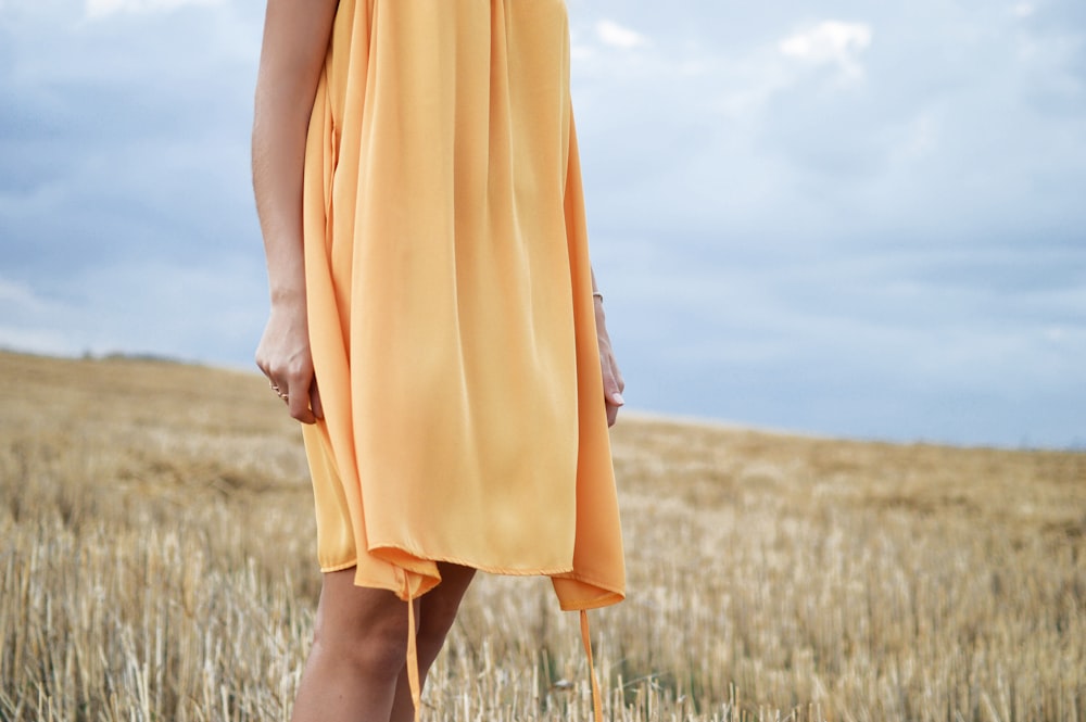 Mujer con vestido amarillo de pie en el campo de hierba verde