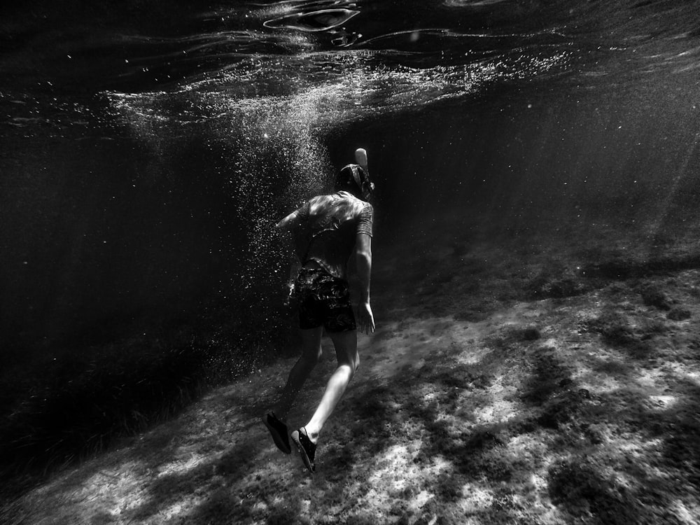 grayscale photography of man swimming underwater