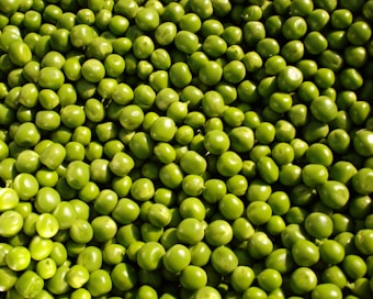 A large collection of fresh green peas tightly packed together. The peas are glossy and vibrant, suggesting freshness and natural texture.