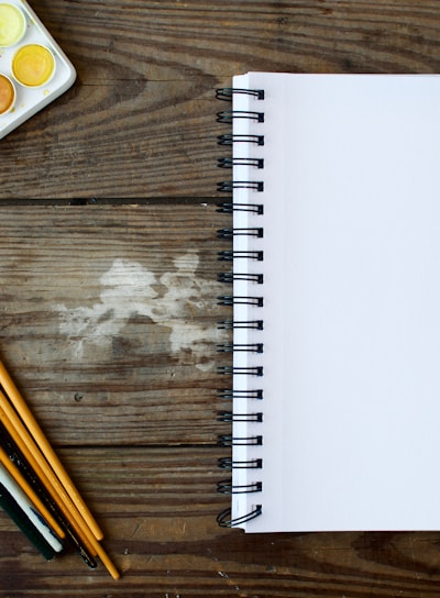 paint brushes next to drawing book and water color palette