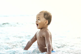 A child splashing water happily near the edge of the sea under a bright blue sky