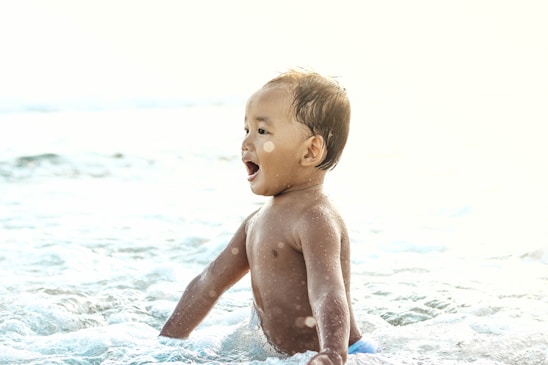 A joyful child gently touching a dolphin in calm ocean waters during a sunny day.