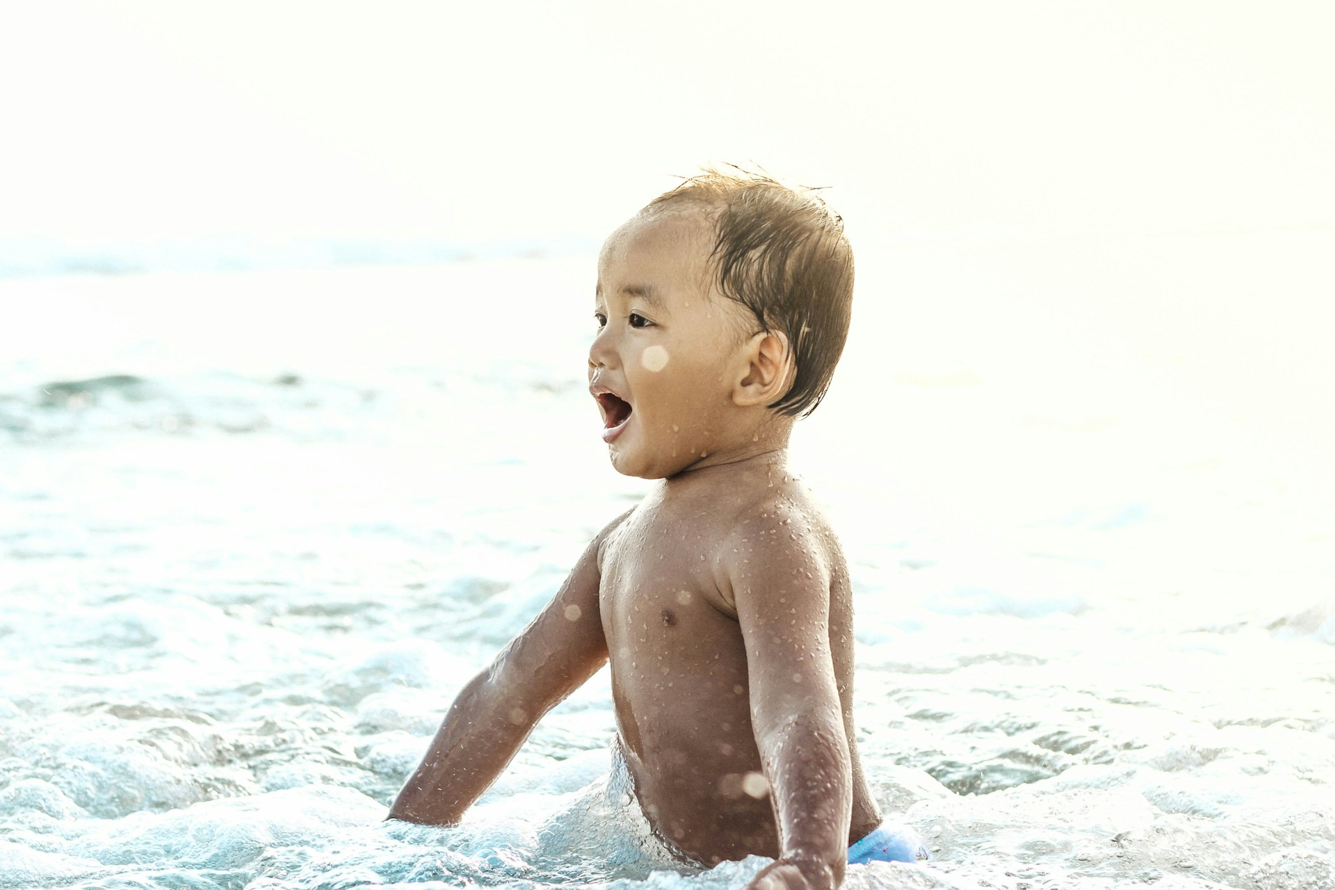 A close-up of a child's laughter amidst beach play, with soft sand and ocean waves in the background.