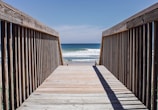 A family walking along a wooden boardwalk toward the ocean under a bright blue sky