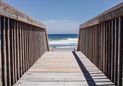A family walking along a wooden boardwalk toward the ocean under a bright blue sky