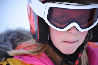 Close-up of hands adjusting ski goggles on a snowy mountain backdrop.