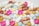 A variety of colorful pills and capsules are scattered across a surface. The assortment includes round, oval, and cylindrical shapes in shades of white, pink, yellow, orange, red, and blue.