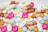 A variety of colorful pills and capsules are scattered across a surface. The assortment includes round, oval, and cylindrical shapes in shades of white, pink, yellow, orange, red, and blue.