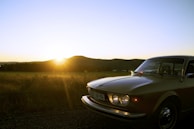 A scenic photo of a couple standing beside their classic car on a winding country road at sunset.